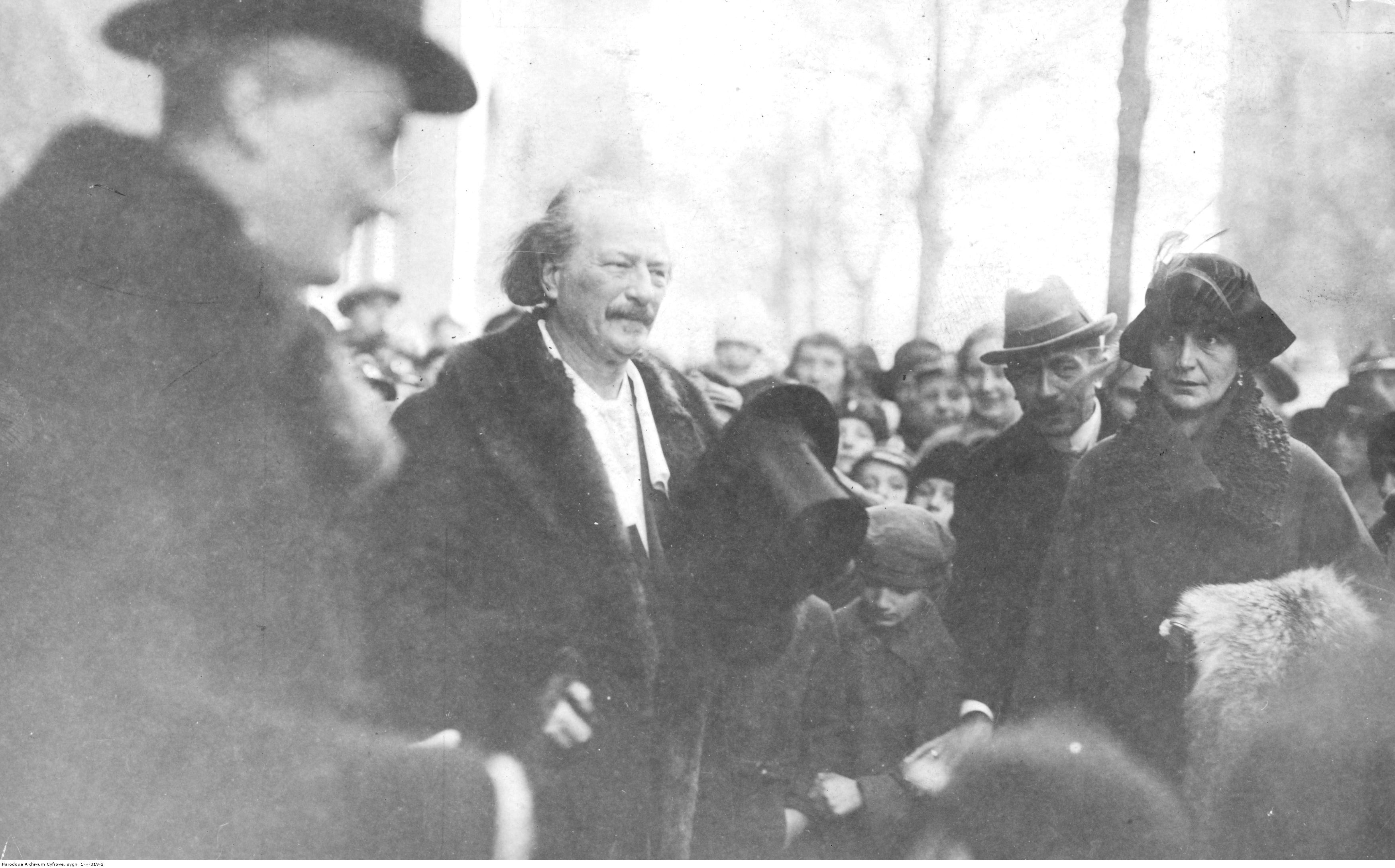 fotografia przedstawiajaca Paderewskiego z cylinderw w dłoni wśród kobiet, mężczyzn i dzieci